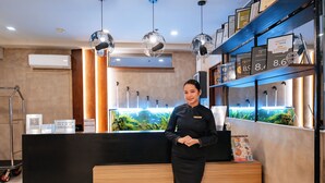 Un mostrador de recepción con una superficie negra, una placa con nombre y un código QR. En la pared hay certificados enmarcados y una fuente decorativa al fondo.