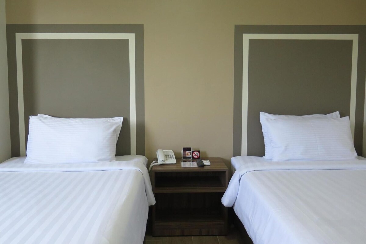 A hotel room with two beds, each with white linens, and a wooden nightstand between them.