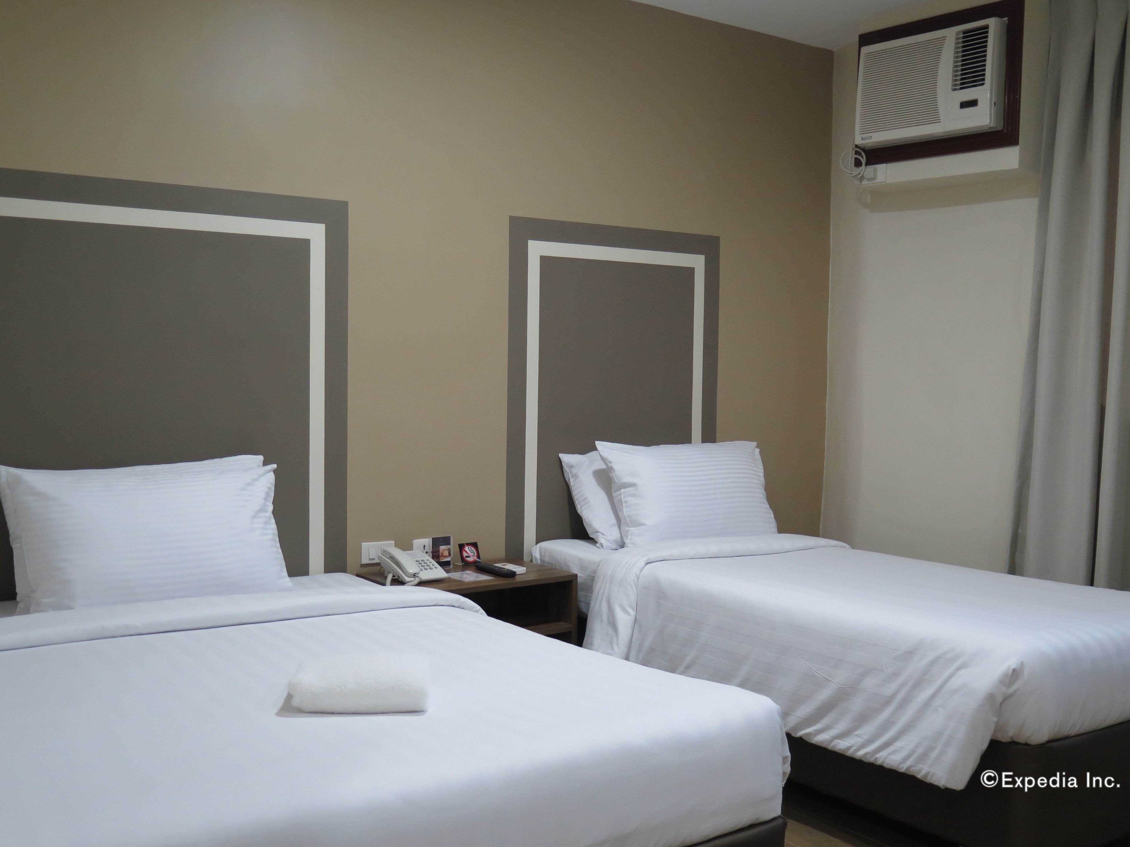 Habitación de hotel con dos camas individuales, una mesita de noche con un teléfono y un control remoto, y un equipo de aire acondicionado instalado en la pared.