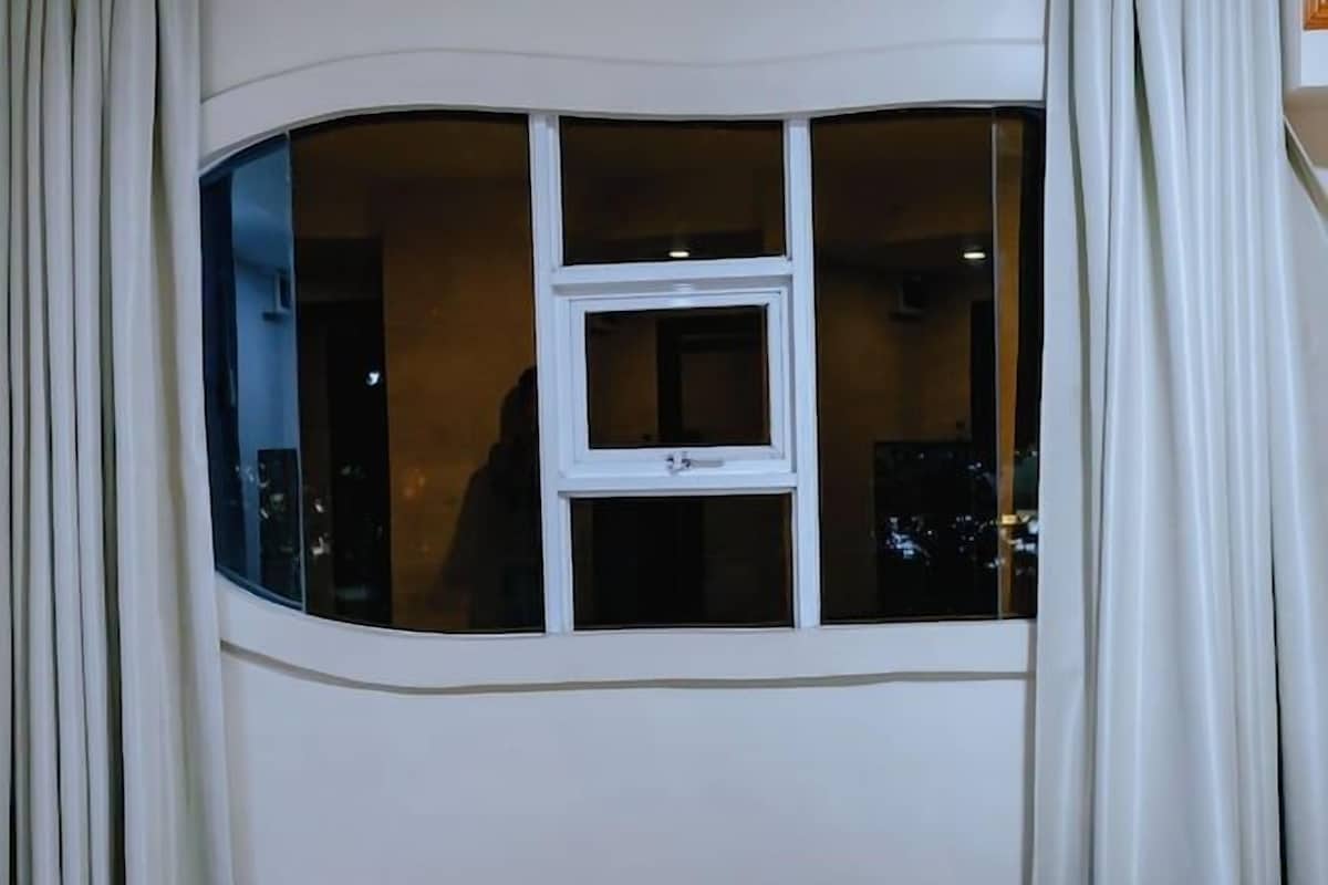 A hotel room with a curved window, curtains, a bed, and a wooden floor.