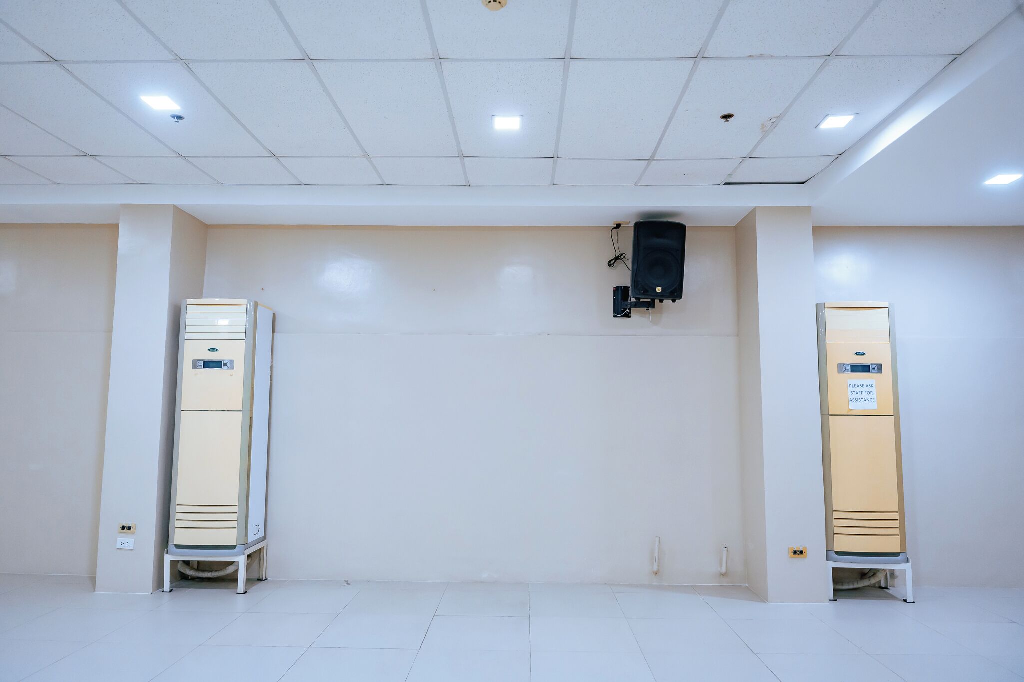 Una habitación con dos taquillas beige, suelo de baldosas blancas y techo blanco con iluminación empotrada.