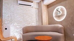 Una sala de estar moderna con un sofá color beige, una mesa de centro redonda de madera, una silla de mimbre y una pared con textura.