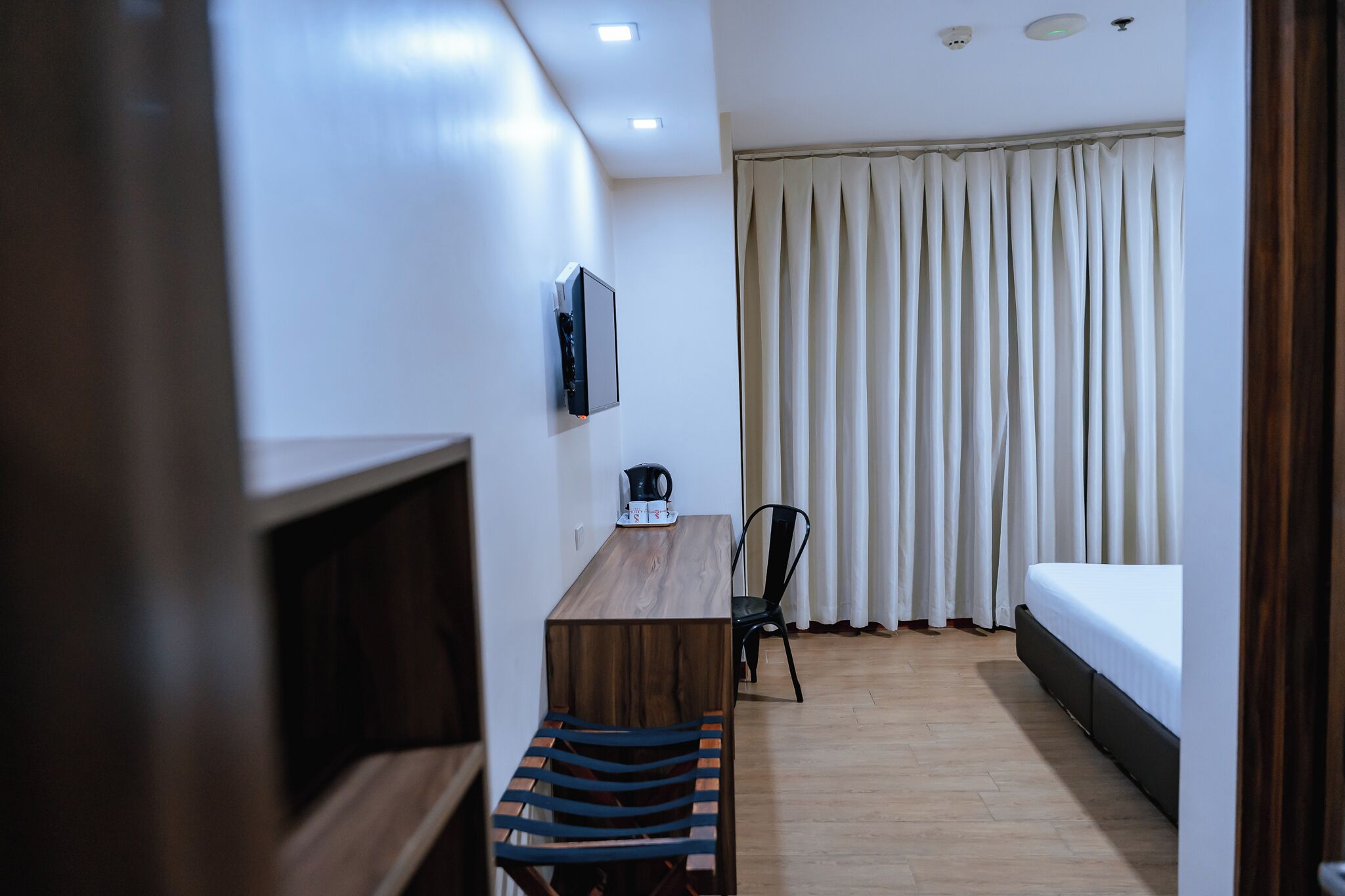 Une chambre d’hôtel moderne avec un bureau en bois, une chaise, un lit et un téléviseur fixé au mur.