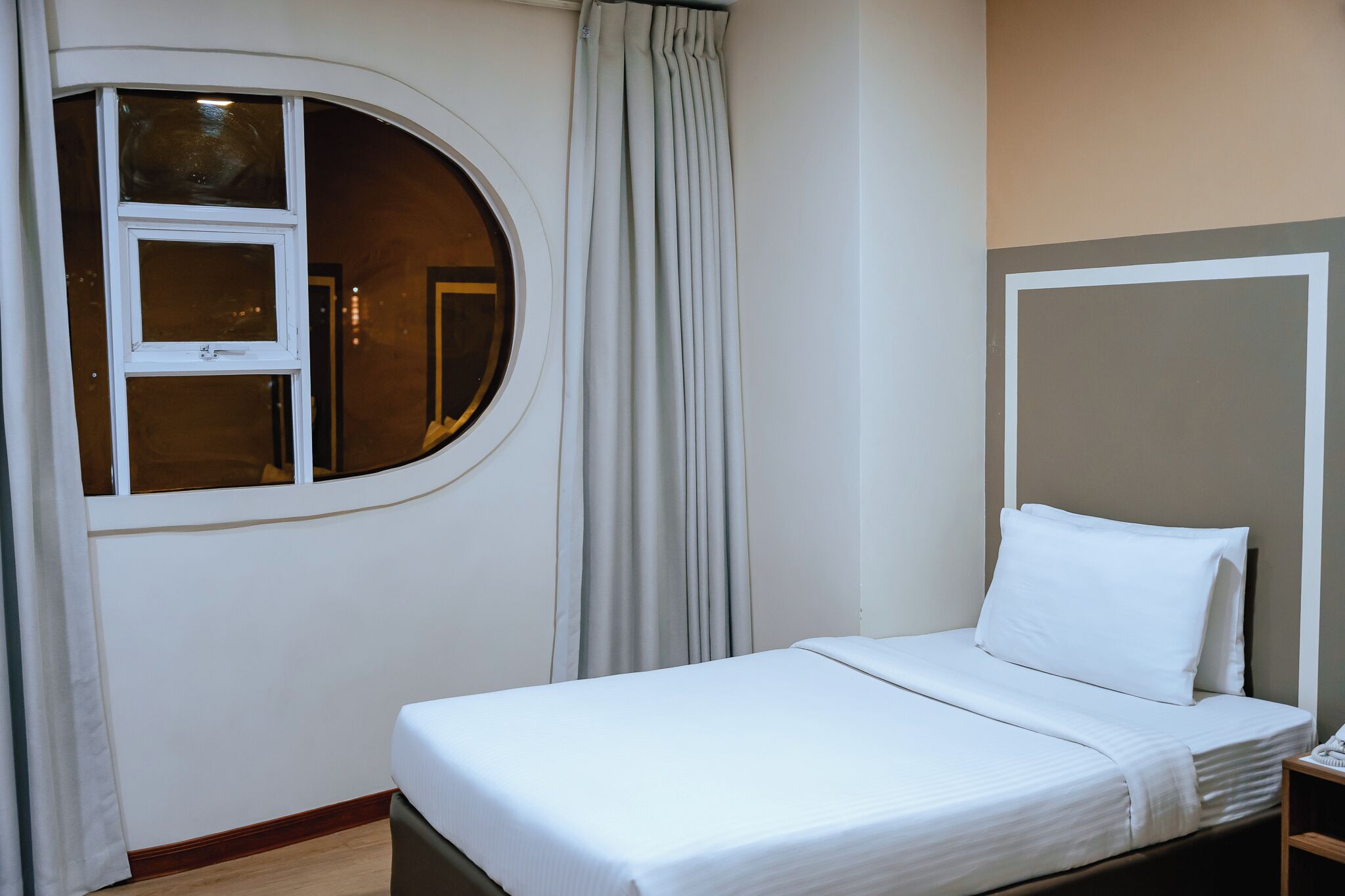 Une chambre d’hôtel avec un lit, une fenêtre ronde et un rideau.