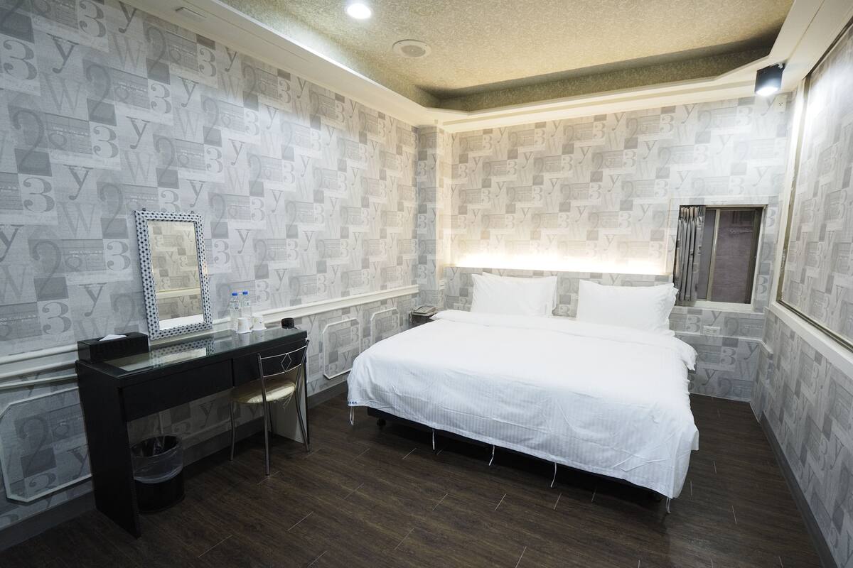 A bedroom with a large bed, a dresser, a mirror, and a window with curtains.