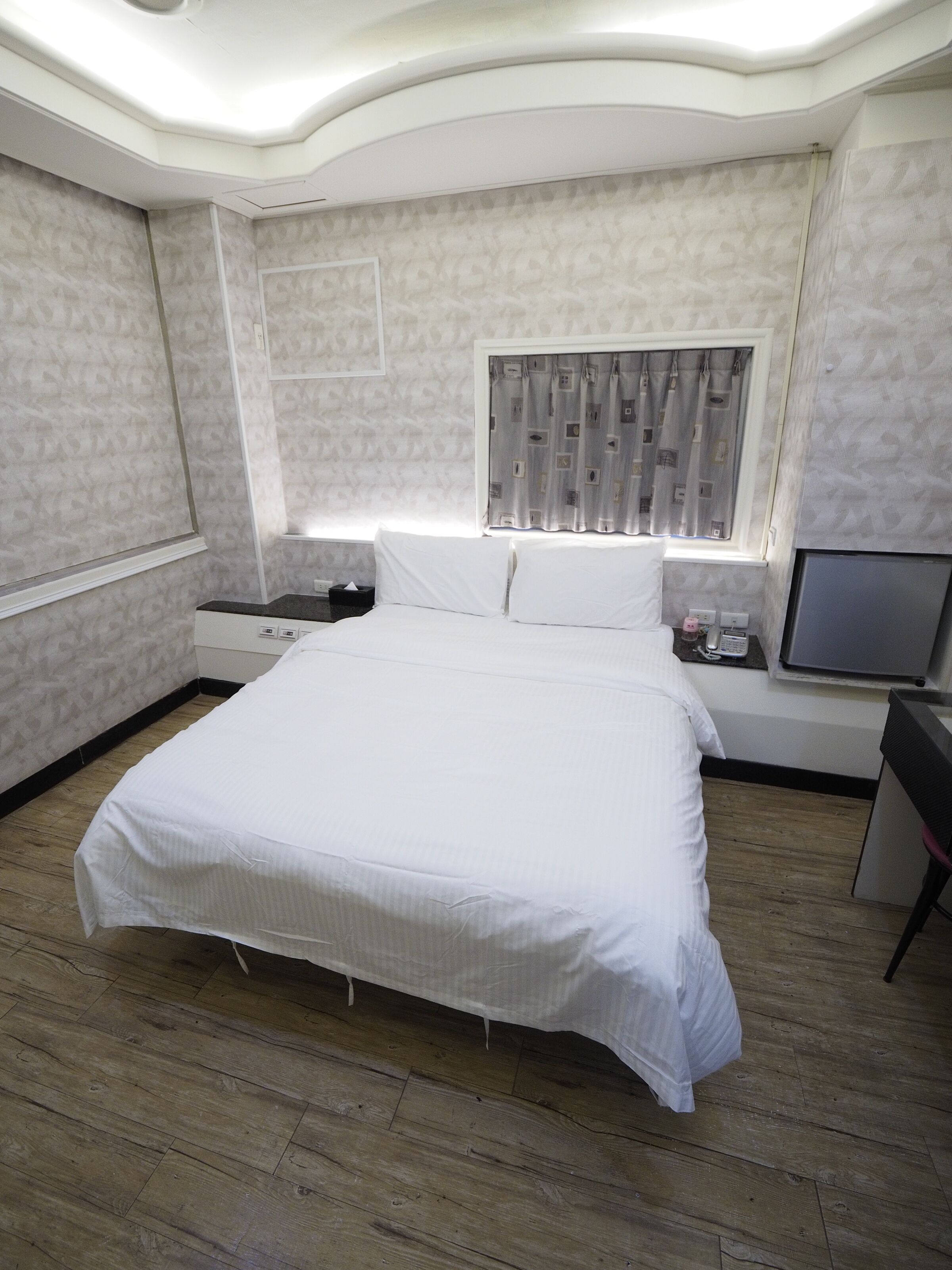 A bedroom with a large bed, a bedside table, a TV, and a window with curtains.