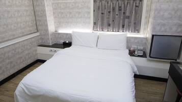 A bedroom with a large bed, a bedside table, a TV, and a window with curtains.