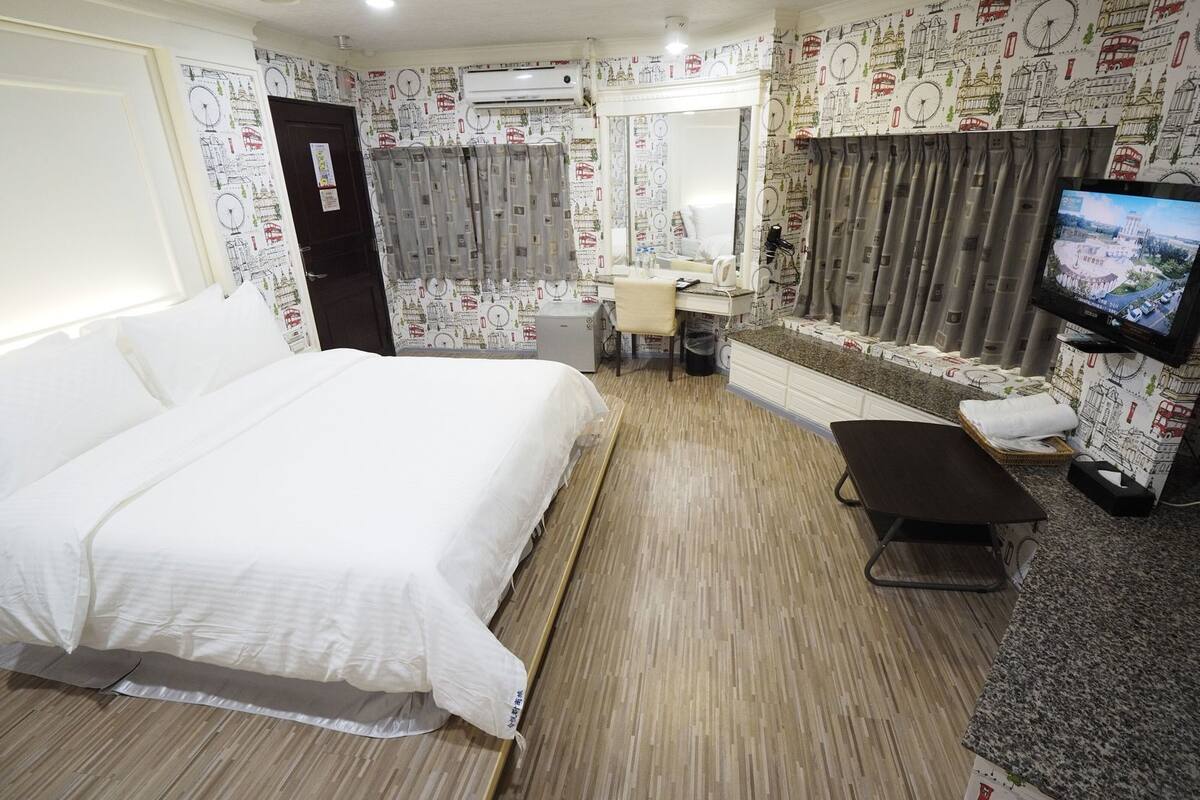 A hotel room with a bed, a desk, a chair, a TV, and a bathroom.