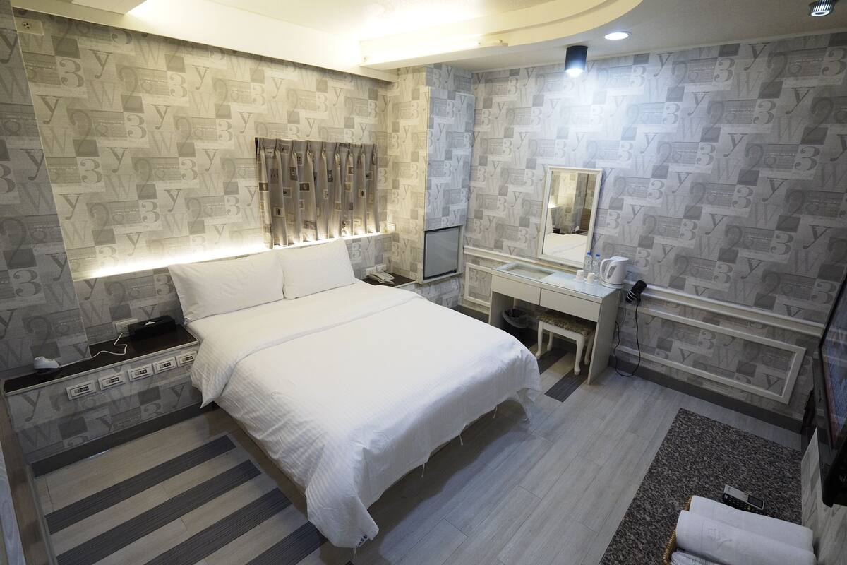 A hotel room with a bed, bedside table, vanity, and a mirror.