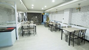 A spacious dining area with multiple tables and chairs, a stone accent wall, and a modern ceiling design. - HeYue Hotel (Hsinchu)