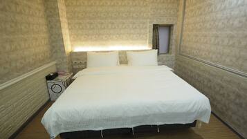A hotel room with a large bed, a bedside table with a lamp, and a small window.