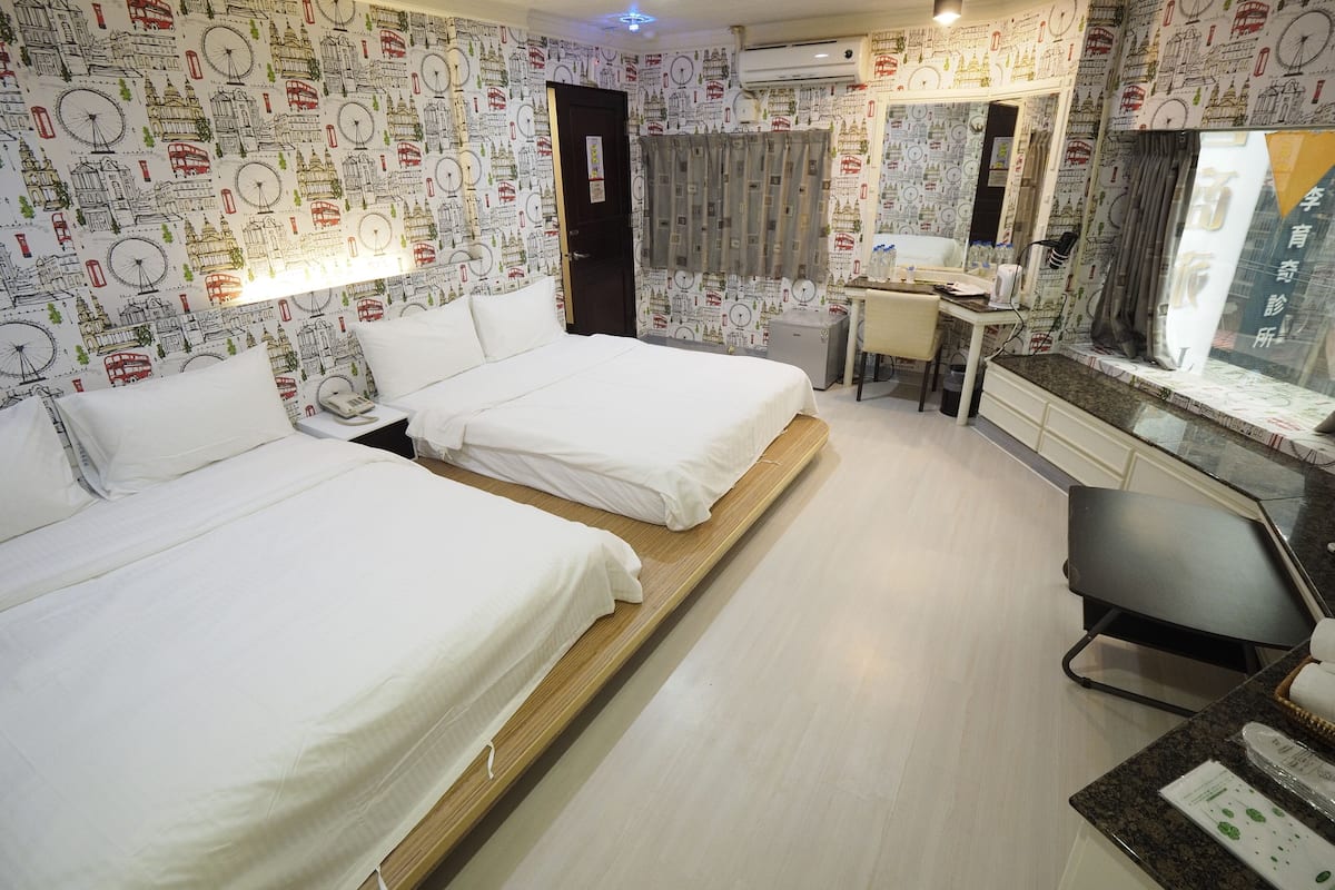 A hotel room with two beds, a desk, and a large window.