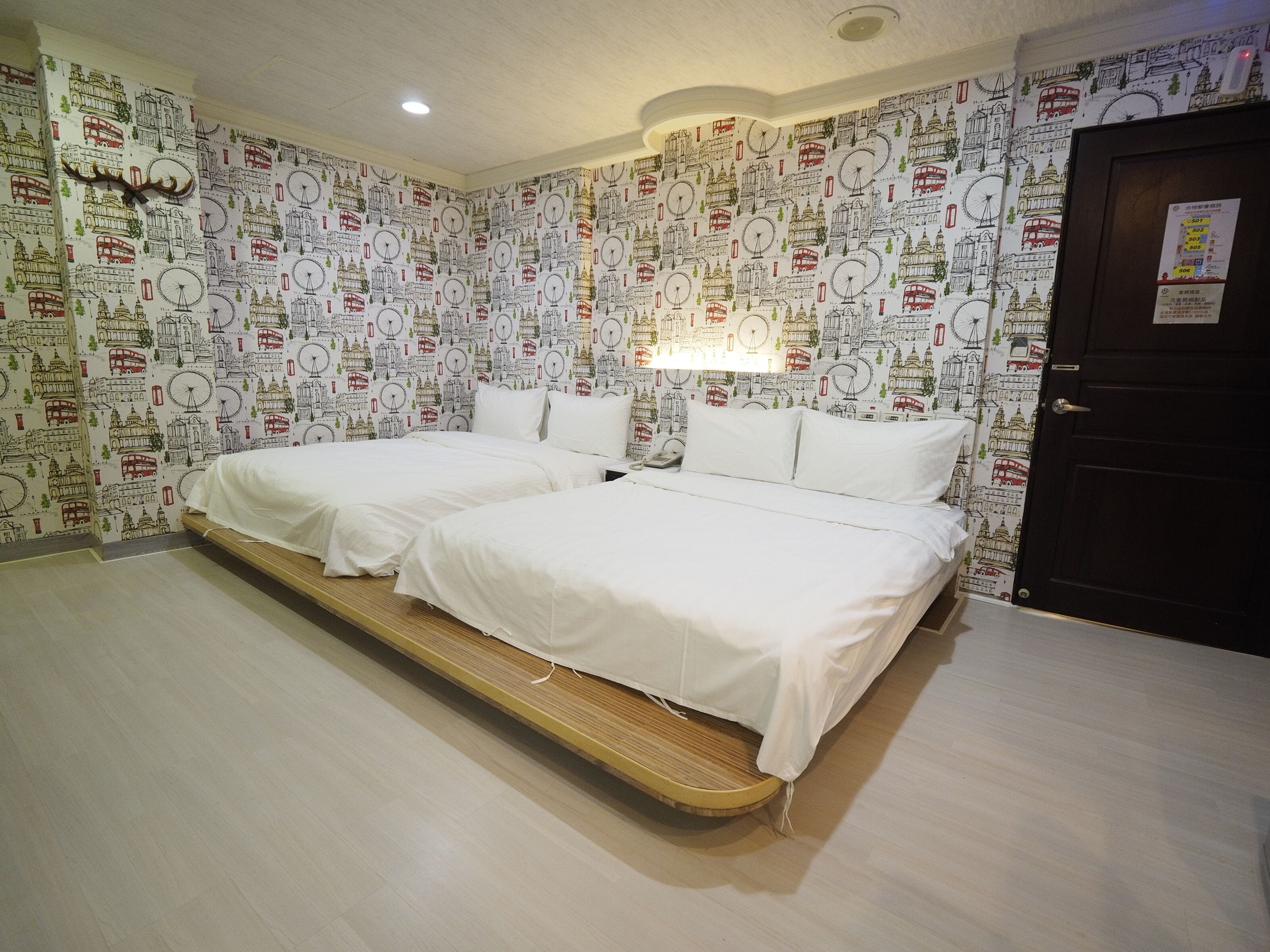 A room with two beds, a wooden platform, and a wall with a travel-themed wallpaper.