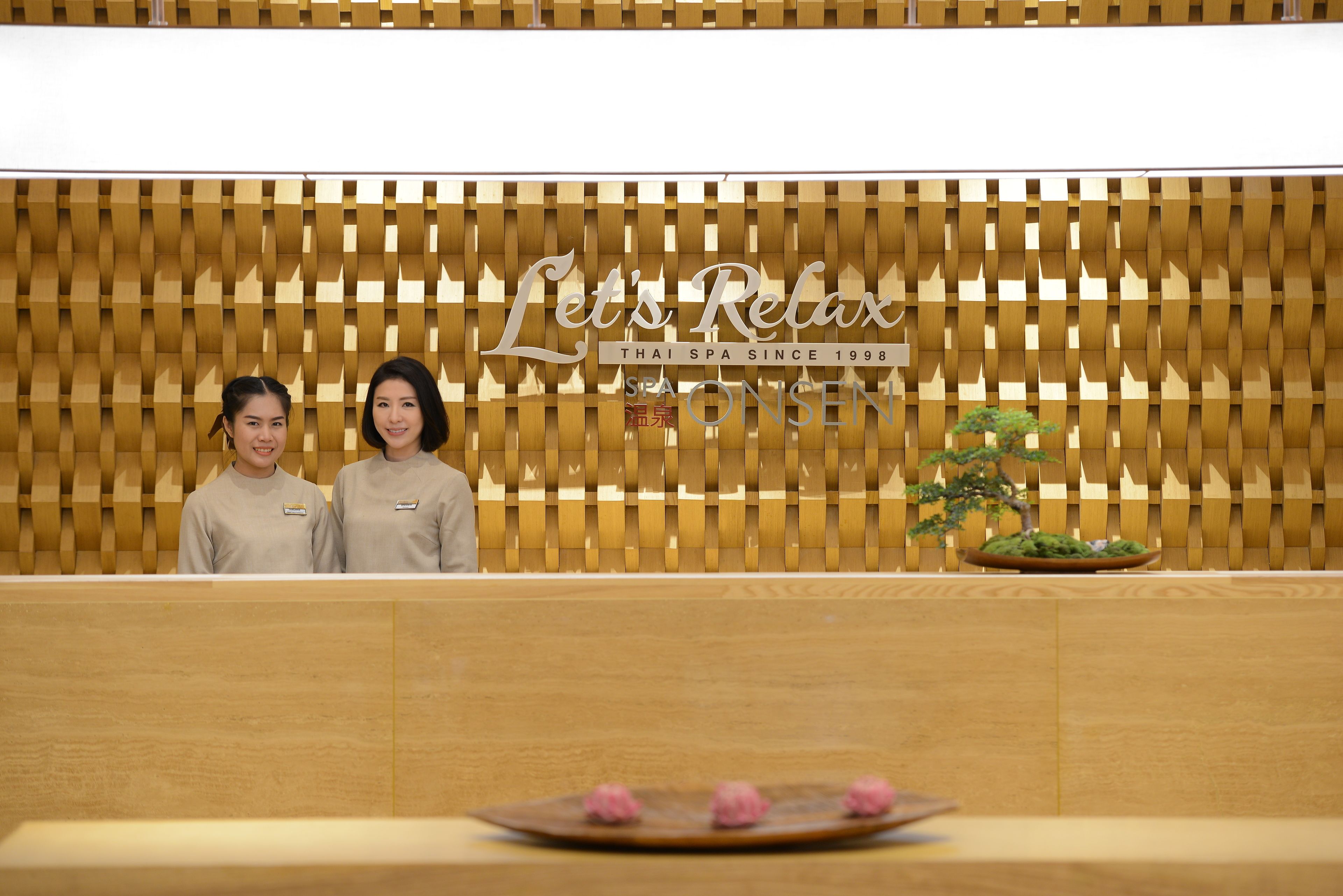 A reception area with a wooden wall and a sign that reads "Let's Relax Thai Spa Since 1998."