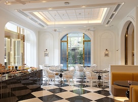 A hotel lobby with a checkered floor, white furniture, a buffet area, and a large arched window.