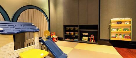 A children's play area with a slide, playhouse, and shelves with books.