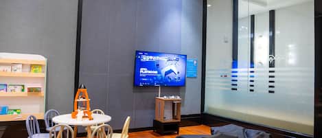 Una sala de juegos con televisor, sillas de madera, una mesita y un sillón de peluche.