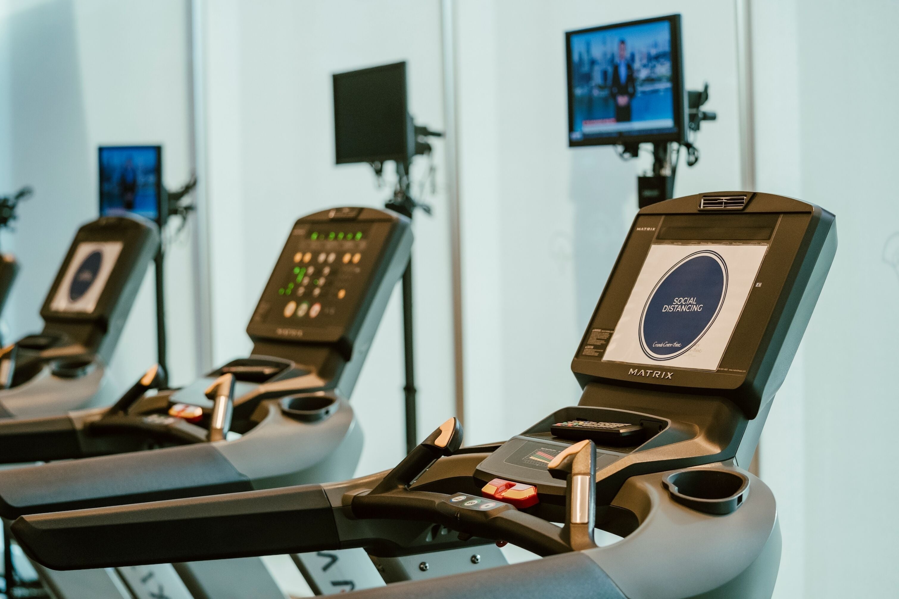 A row of stationary bikes with digital displays and a screen above each, indicating a fitness or exercise area.
