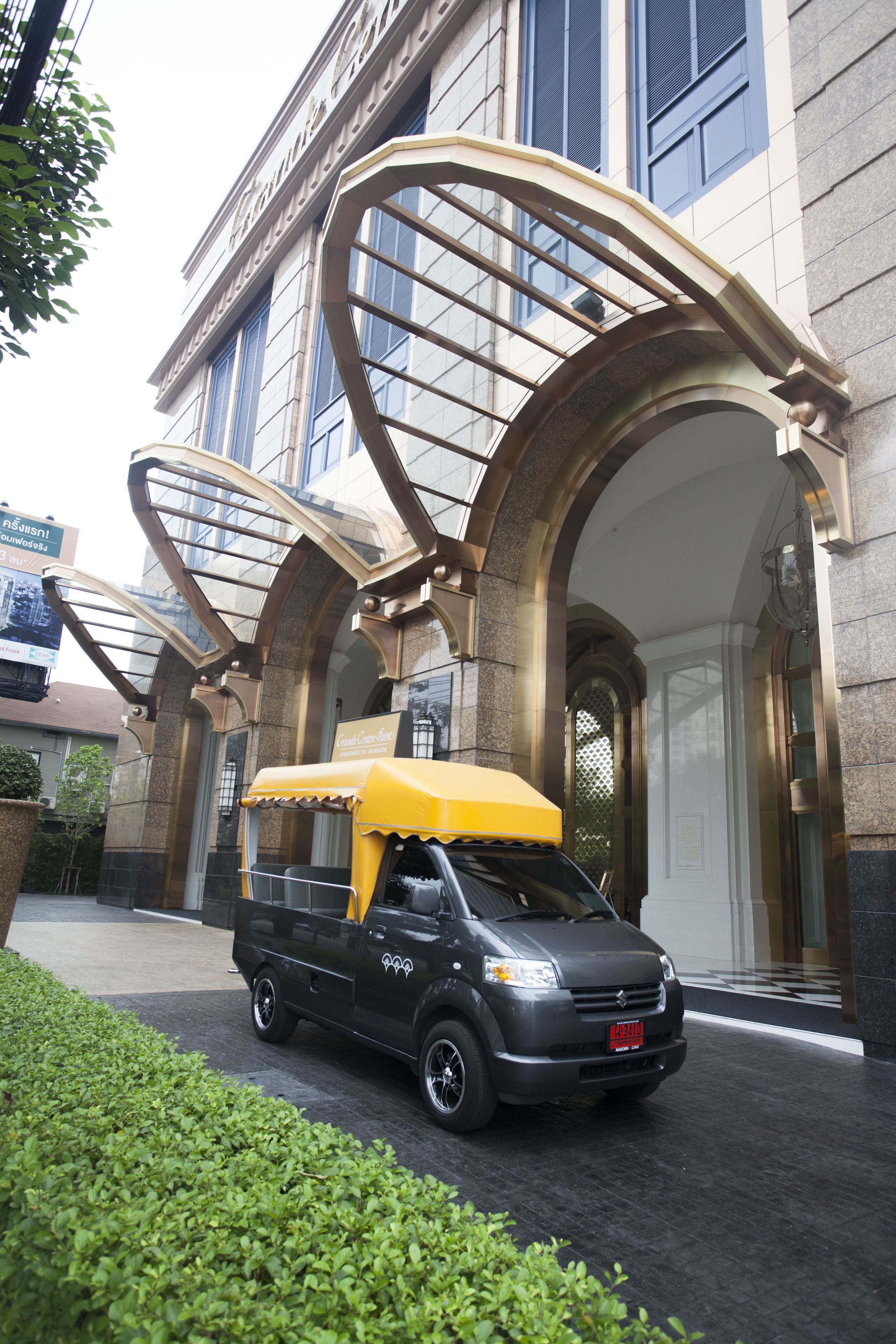 Un furgone nero con tenda gialla parcheggiato di fronte a un edificio con ampie finestre ad arco e facciata in pietra.