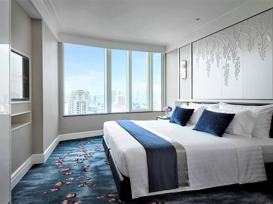 A hotel room with a large bed, a city view, and a decorative wall panel.