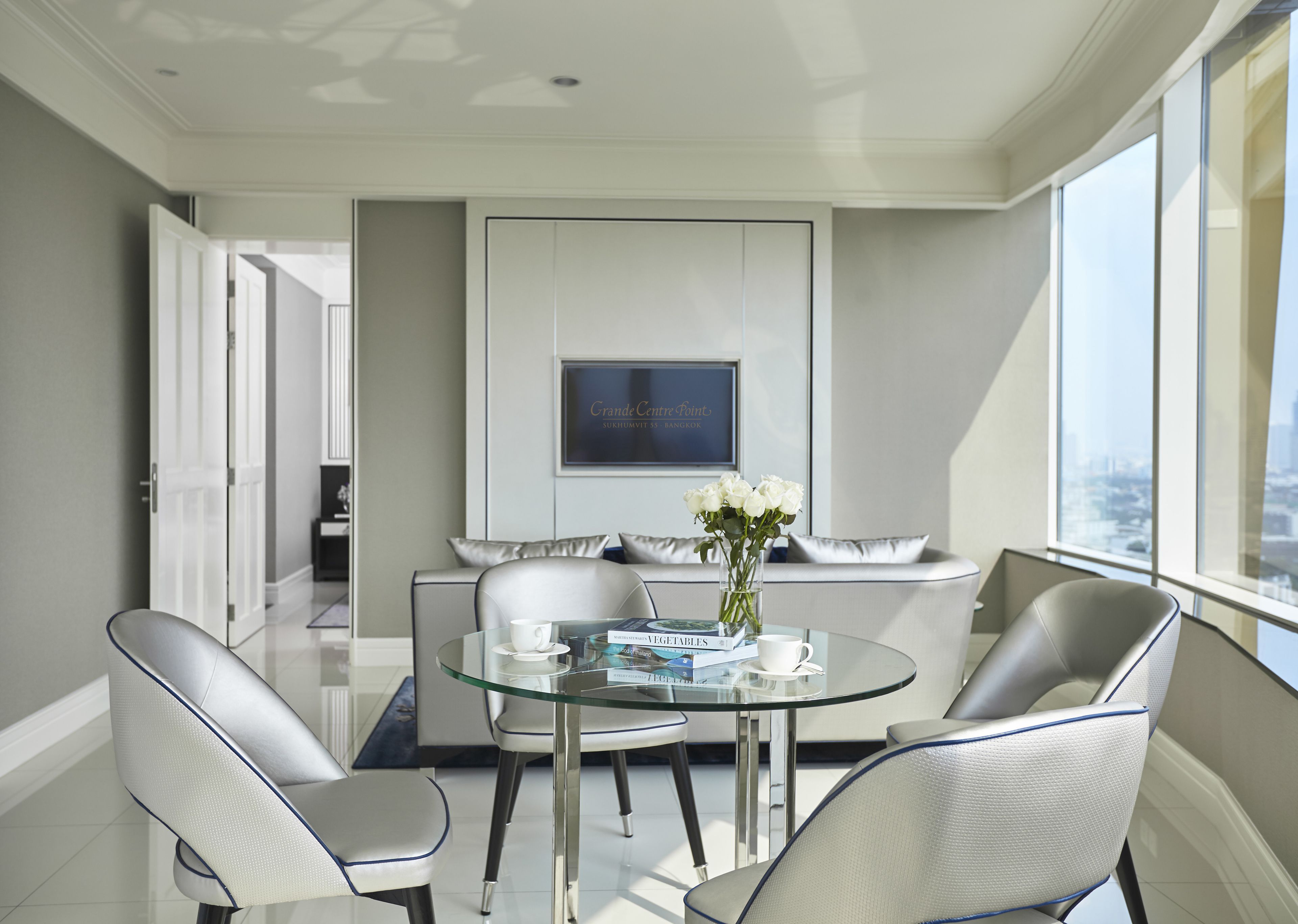 A modern dining area with a glass table, white chairs, and a vase of white flowers.