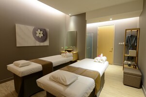 Hotelkamer met twee bedden, een grote spiegel, een opbergkapstok en een klein tafeltje met een schaal en bloemen.