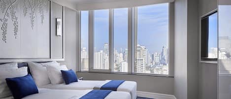 Habitación de hotel con dos camas, ventanas amplias, vistas a la ciudad y alfombra estampada.