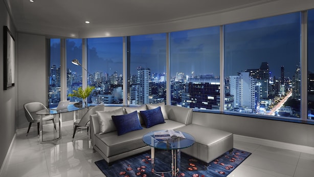 A modern living room with a city view, a sofa, a glass coffee table, and a dining area with chairs. - Grande Centre Point Sukhumvit 55 (Bangkok)