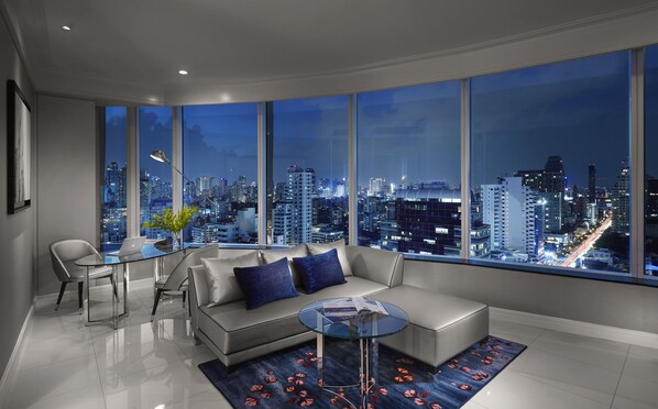 Una sala de estar moderna con vista a la ciudad, un sofá, una mesa de centro de cristal y un comedor con sillas.