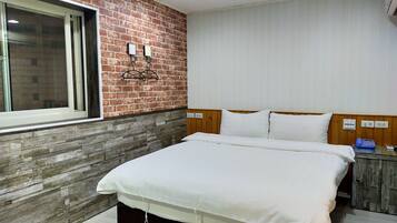 Ein Hotelzimmer mit Backsteinwand, einem Holzkopfteil, einem großen Bett mit weißen Leinen, einem Nachttisch mit Telefon und einem Fenster mit Jalousien.