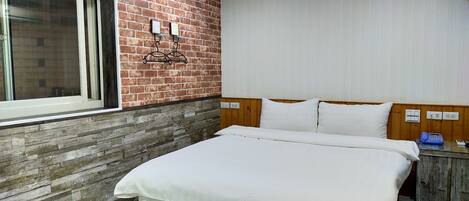 Habitación de hotel con pared de ladrillo decorativa, cabecera de madera, cama grande con ropa blanca, mesita de noche con teléfono y ventana con persianas.