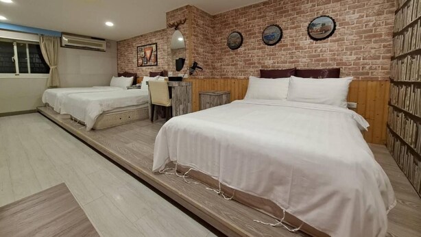 Une chambre d’hôtel avec deux lits, un bureau et un mur en briques.