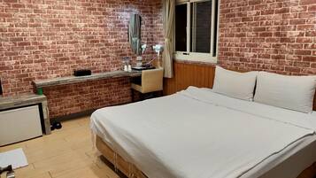 Habitación de hotel con pared de ladrillo, cama de madera, escritorio con silla, ventana y espejo.