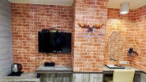 Une cuisine compacte avec un mur en briques, un téléviseur fixé au mur, un petit réfrigérateur, un comptoir en bois et une chaise.