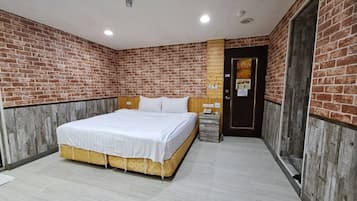 A hotel room with a brick wall, a wooden headboard, a bed with white bedding, a nightstand, and a door with a sign.
