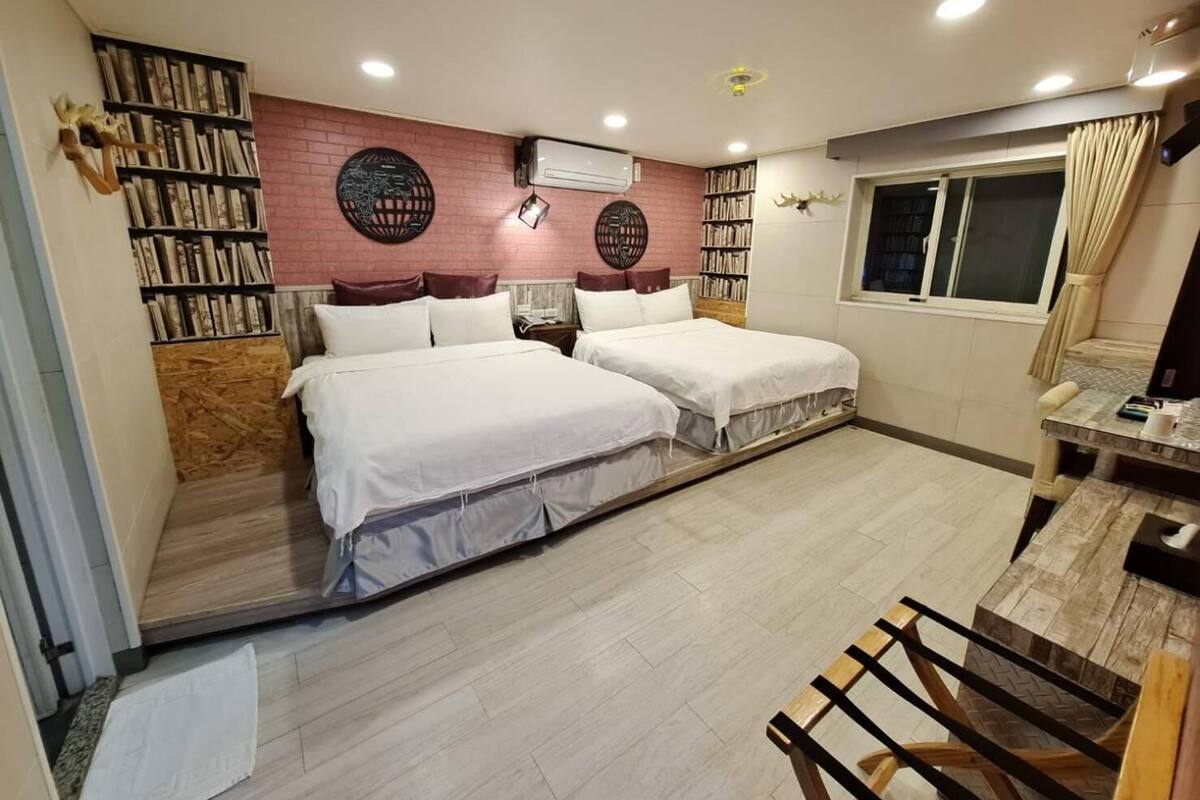 Une chambre avec deux lits, une bibliothèque, un appareil de climatisation et une fenêtre avec des rideaux.