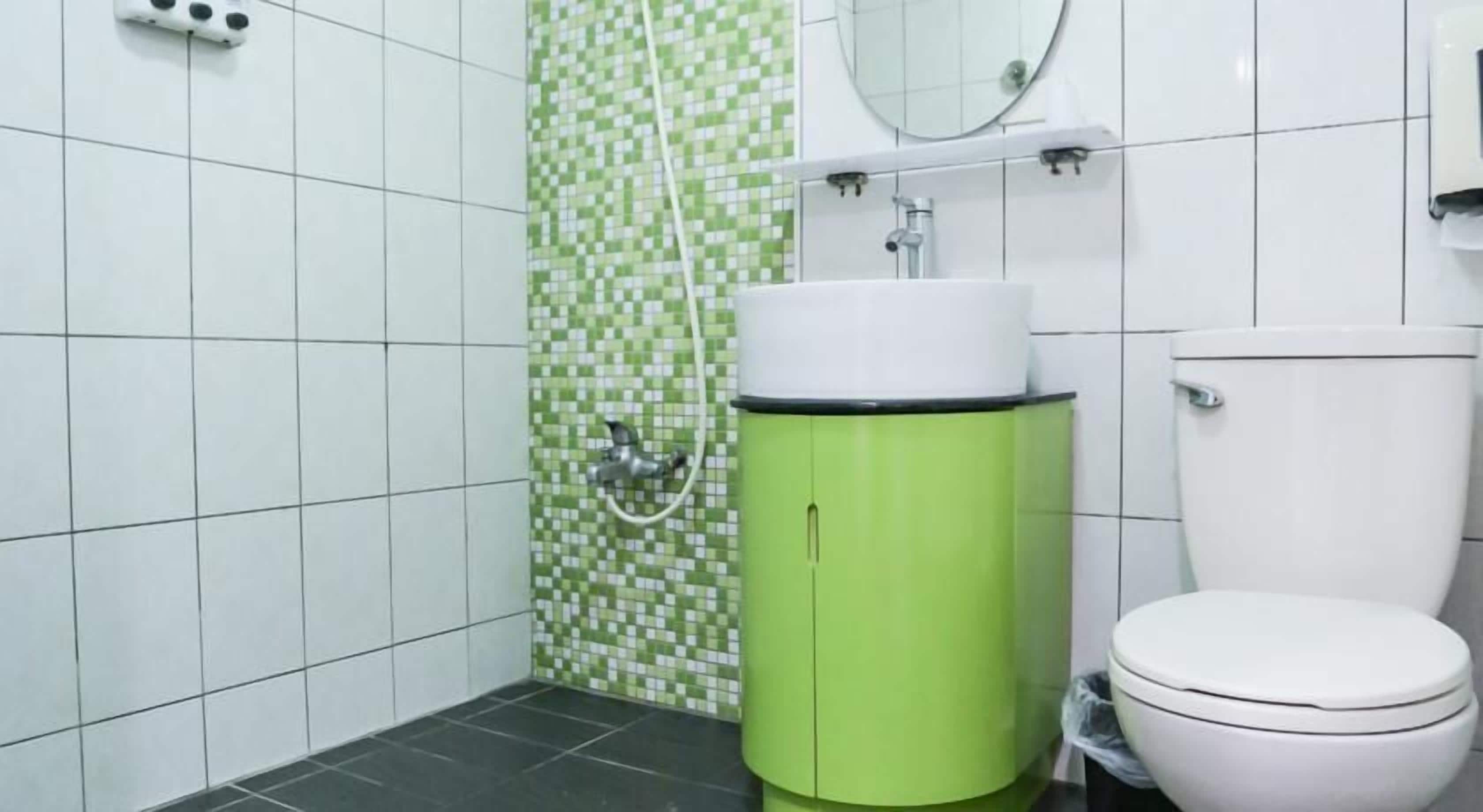 A bathroom with a green sink, white toilet, and a shower with a green and white tiled wall.