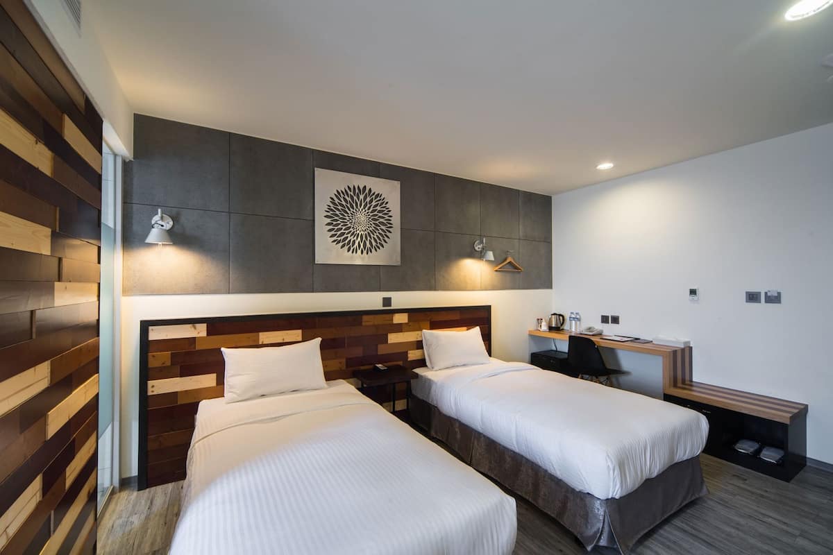 Une chambre d’hôtel avec deux lits, un bureau, une chaise, une machine à café et une œuvre d’art accrochée au mur.