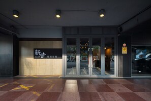 Entrada de hotel con puerta de cristal, un letrero con caracteres chinos y suelo de baldosas.