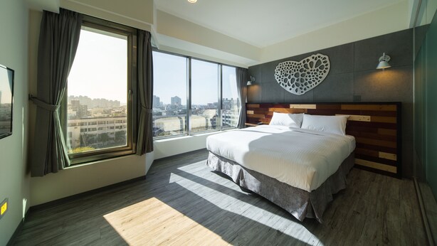 Une chambre d’hôtel moderne dotée d’un grand lit, offrant une vue sur la ville et agrémentée d’une décoration murale originale.