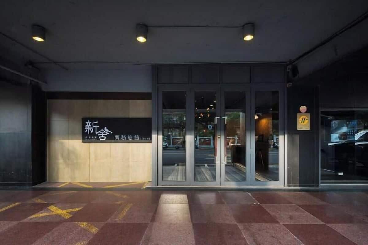 L’entrée d’un hôtel, avec une porte en verre, une enseigne avec des caractères chinois et un sol carrelé.