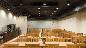 Un grand espace dédié à la salle à manger, avec de nombreuses tables et chaises en bois, un comptoir équipé d’appareils de cuisine et des luminaires suspendus.