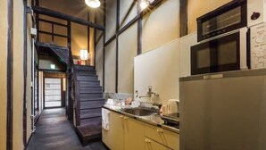 A narrow kitchen with a stainless steel refrigerator, a microwave, and a sink. A wooden staircase leads to another room. - Traditional Kyoto Home Bifuku Roujiya (Kyoto)