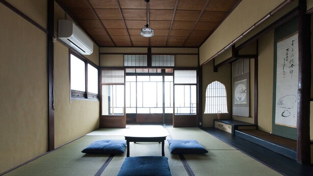 A traditional Japanese room with tatami flooring, a low table, cushions, sliding doors, and a hanging scroll.