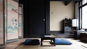 A traditional Japanese room with tatami flooring, a low wooden table, cushions, and a sliding door with artwork.