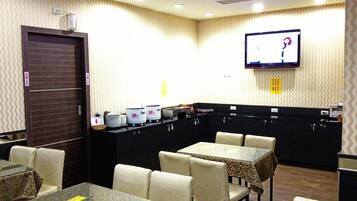 A hotel room with a dining area, a TV mounted on the wall, and a minibar.