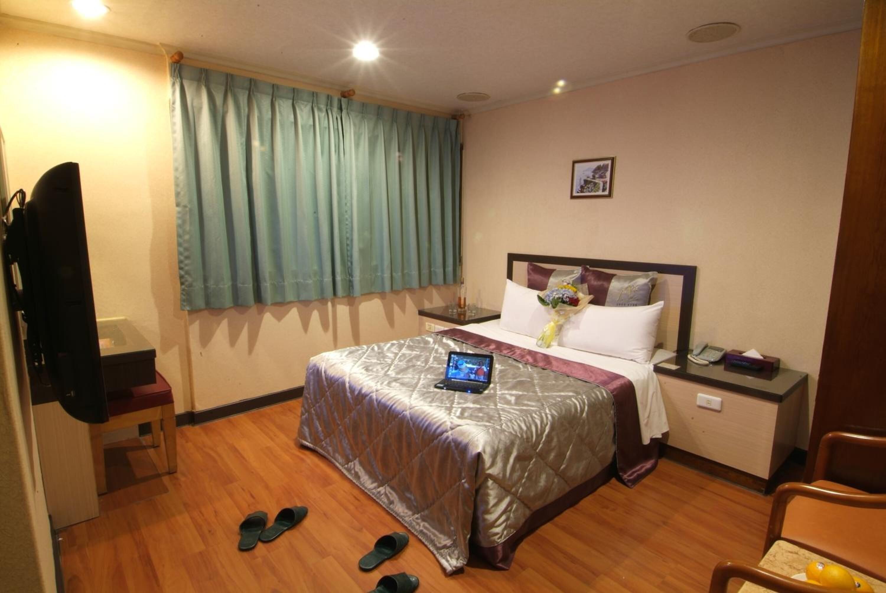 Habitación de hotel con cama, mesita de noche, silla y ventana con cortinas.