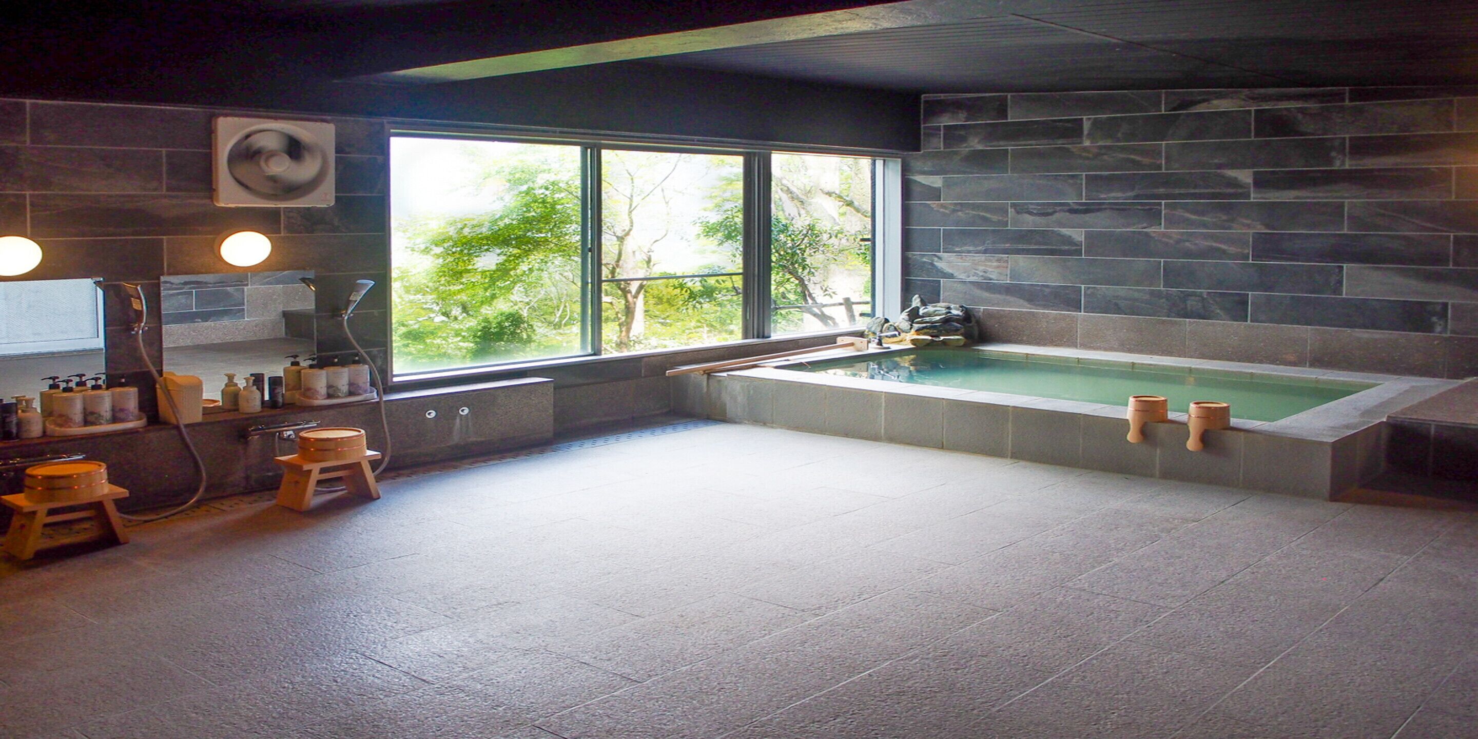 A spacious bathroom with a large bathtub, a window with a view of trees, and a stone wall.