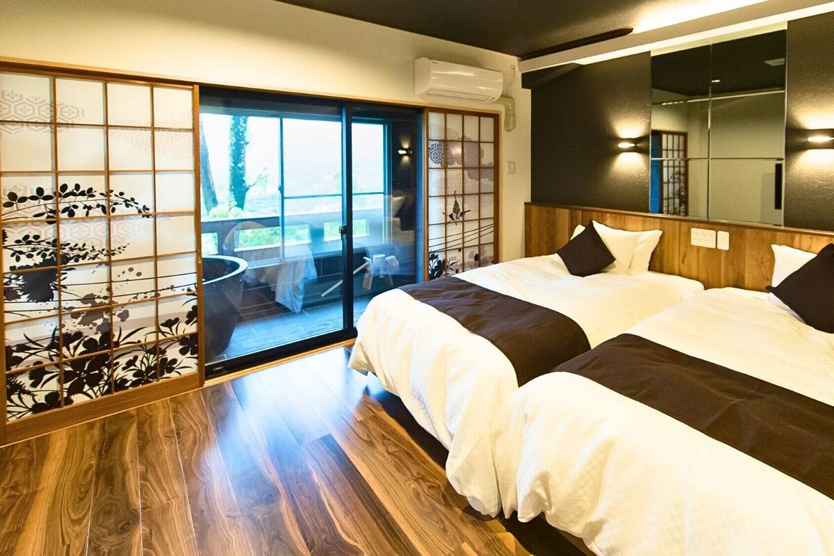 A hotel room with two beds, a sliding glass door leading to a balcony, and a large mirror on the wall.