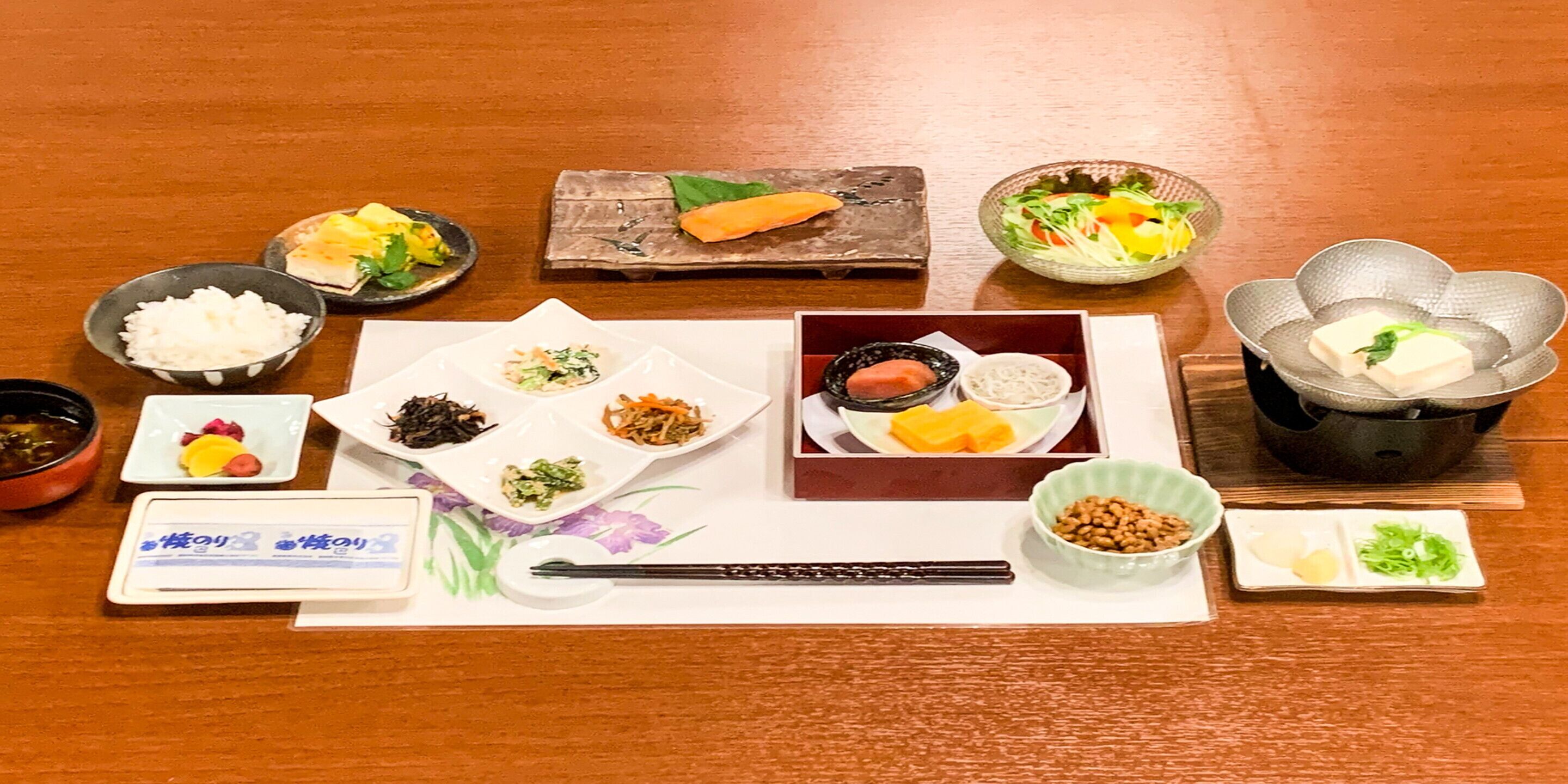 Een traditionele Japanse maaltijdopstelling met diverse gerechten en bestek op een houten tafel.